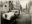 Black-and-white street photograph of a vintage luxury car parked along a historic New Orleans streetscape with pedestrians nearby.