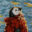 Stylized self-portrait of artist Patrick de Guzman depicted as a penguin wearing a red patterned sweater against a blue sky.