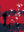 Figure walking among pigeons and white birds taking flight across a bold red urban landscape.