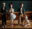 Group of hand-carved marionette characters standing together on a wooden floor, each with distinctive facial features, clothing, and suspended control strings.